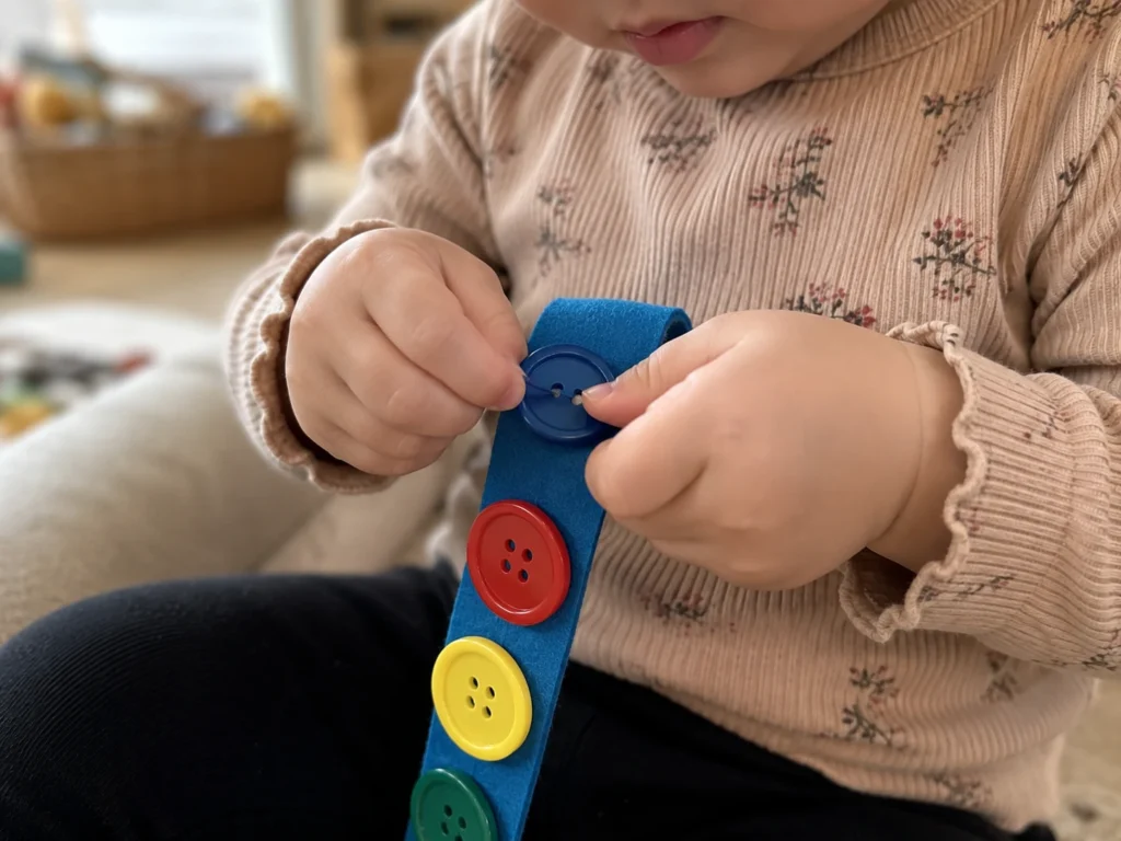 toddler threading large buttons onto a felt button snake